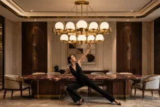 Woman posing beneath a sculptural Art Deco pendant above a burgundy marble dining table