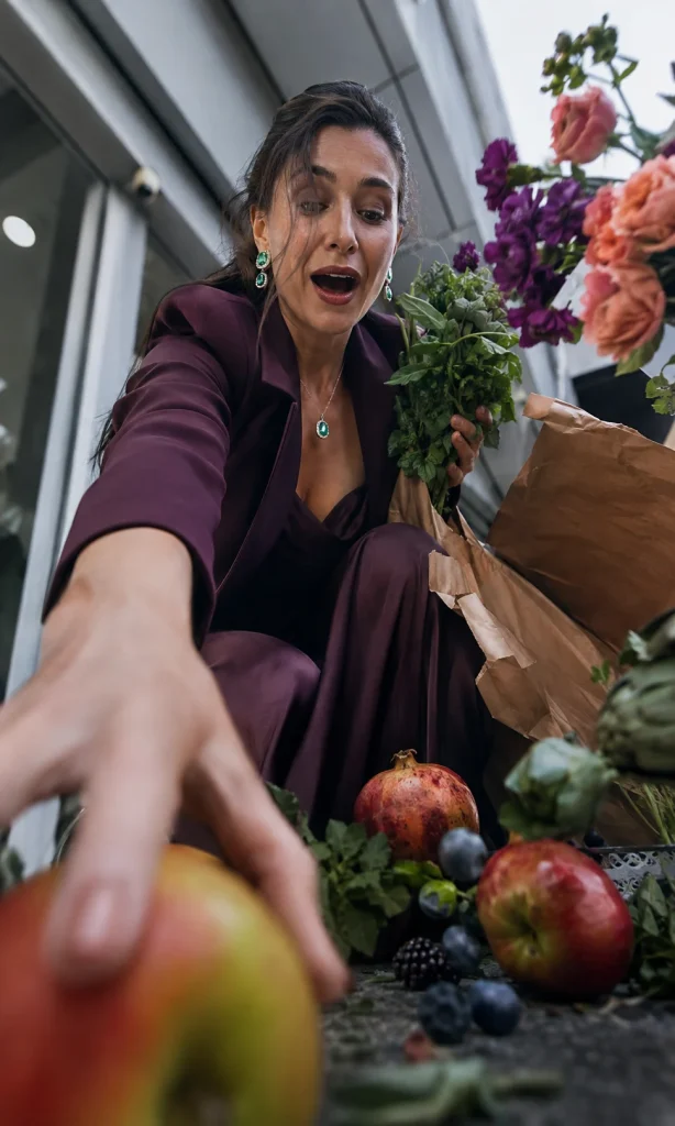 Woman reacting spontaneously as groceries spill from a torn bag outside a supermarket.