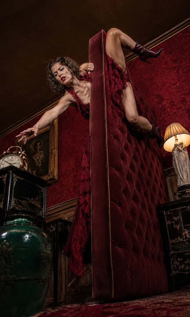Woman climbing over an upright mattress in a dramatic representation of exhaustion and low energy.
