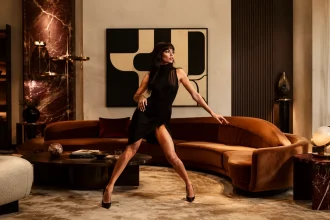Woman posing in a luxurious Neo Deco living room with a curved cognac sofa, walnut, red marble and brass details